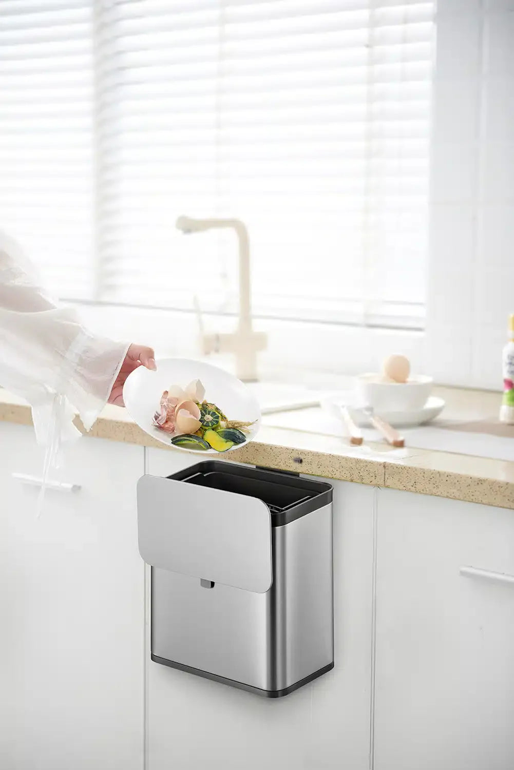 Modern kitchen with a wall-mounted trash can and a person preparing food.